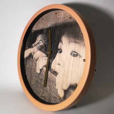 Gatto e bambino esplorano tra tavole di legno: l’orologio da parete li ritrae in un momento unico. Cornice in ecopelle kaki, lancette dorate, stile caldo e suggestivo.
